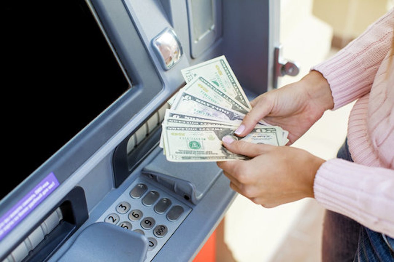 person holding dollar cash in front of an ATM machine